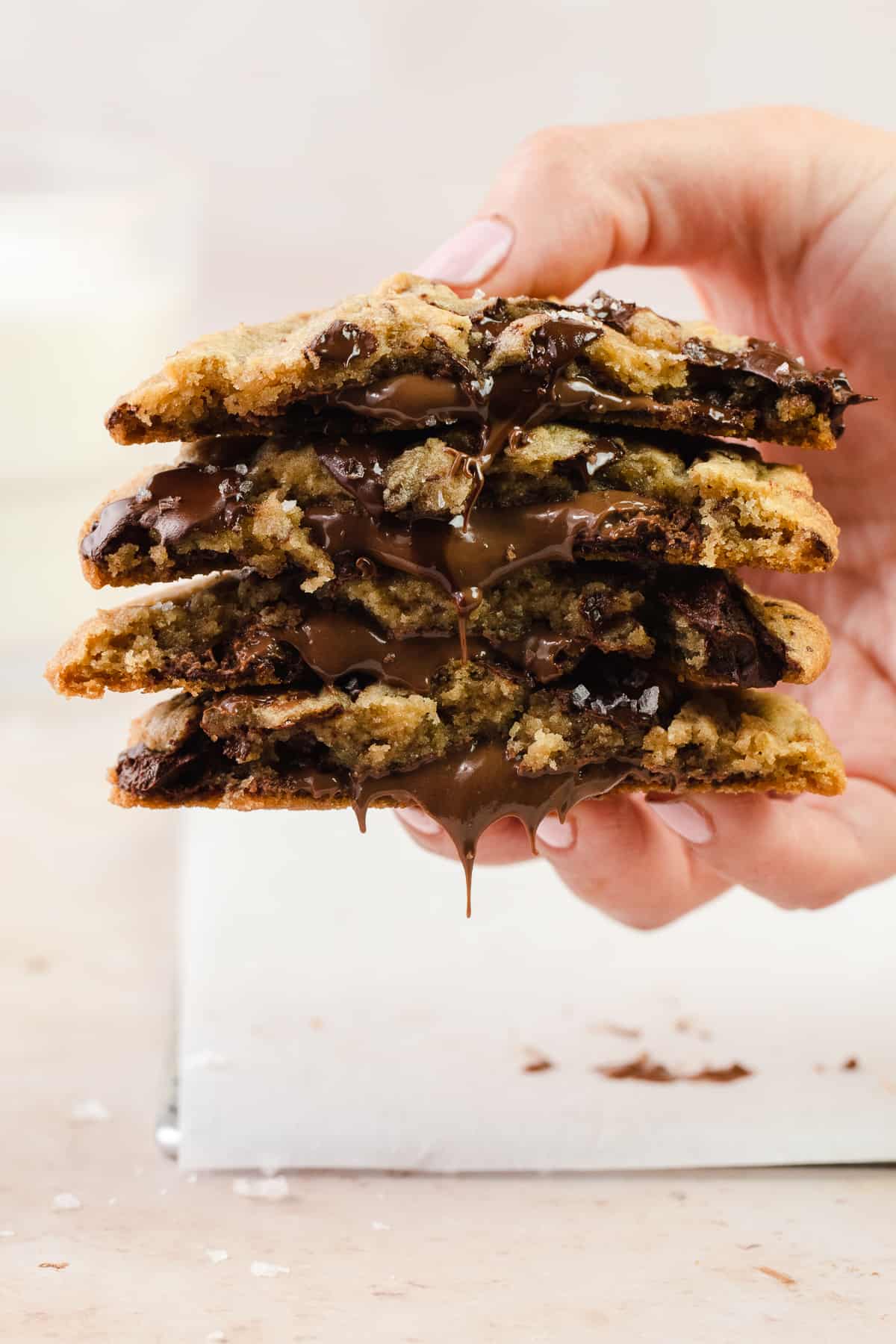 A hand holding a cross section of 4 Nutella Chocolate Chip Cookies with glass of milk in the back