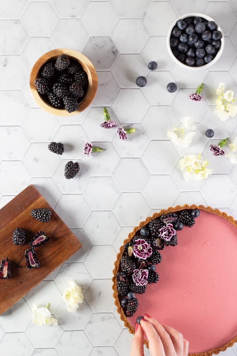 A hand decorating tart with blackberries and blueberries