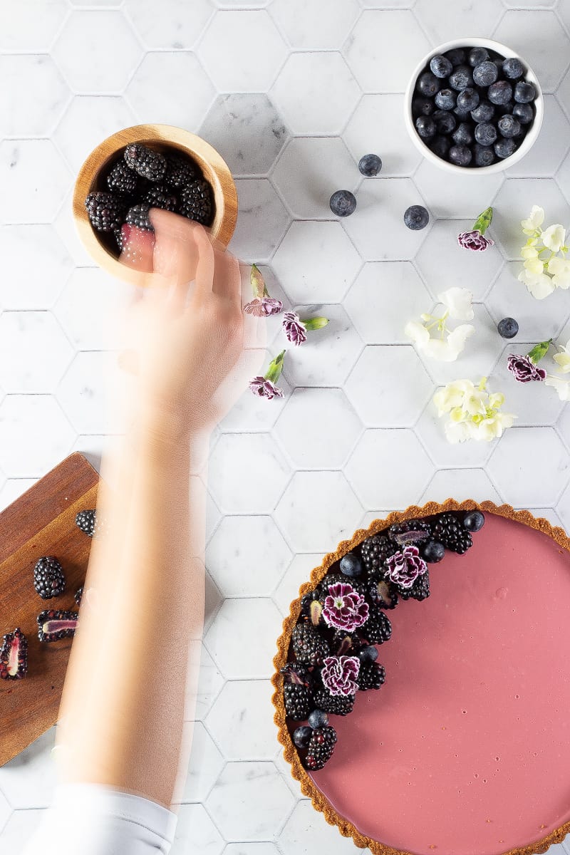 A hand decorating tart with blackberries and blueberries