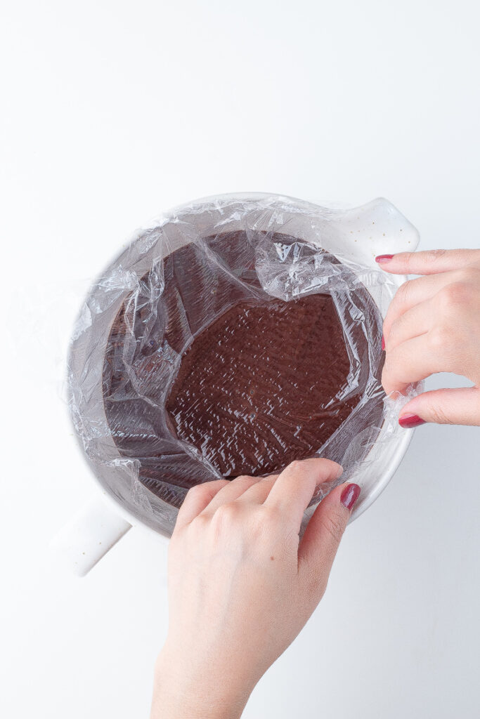 Hands placing plastic wrap on top of chocolate custard