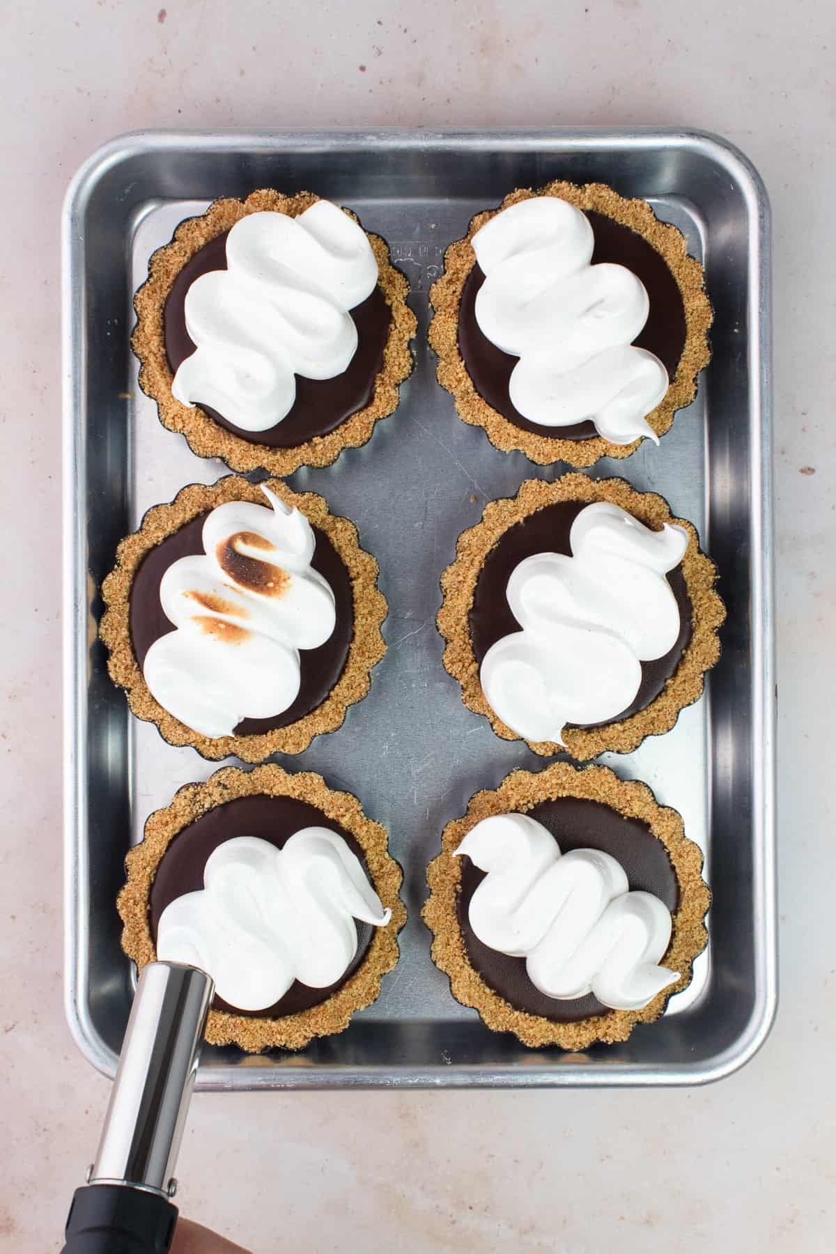 A kitchen torch is torching one of the mini tarts