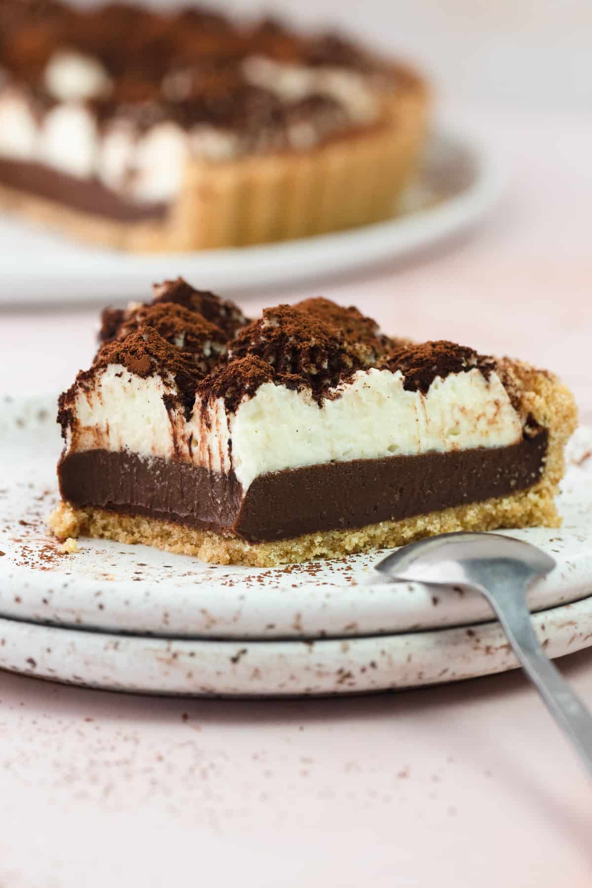 A close up of a slice of tiramisu tart on a plate with a spoon on the side