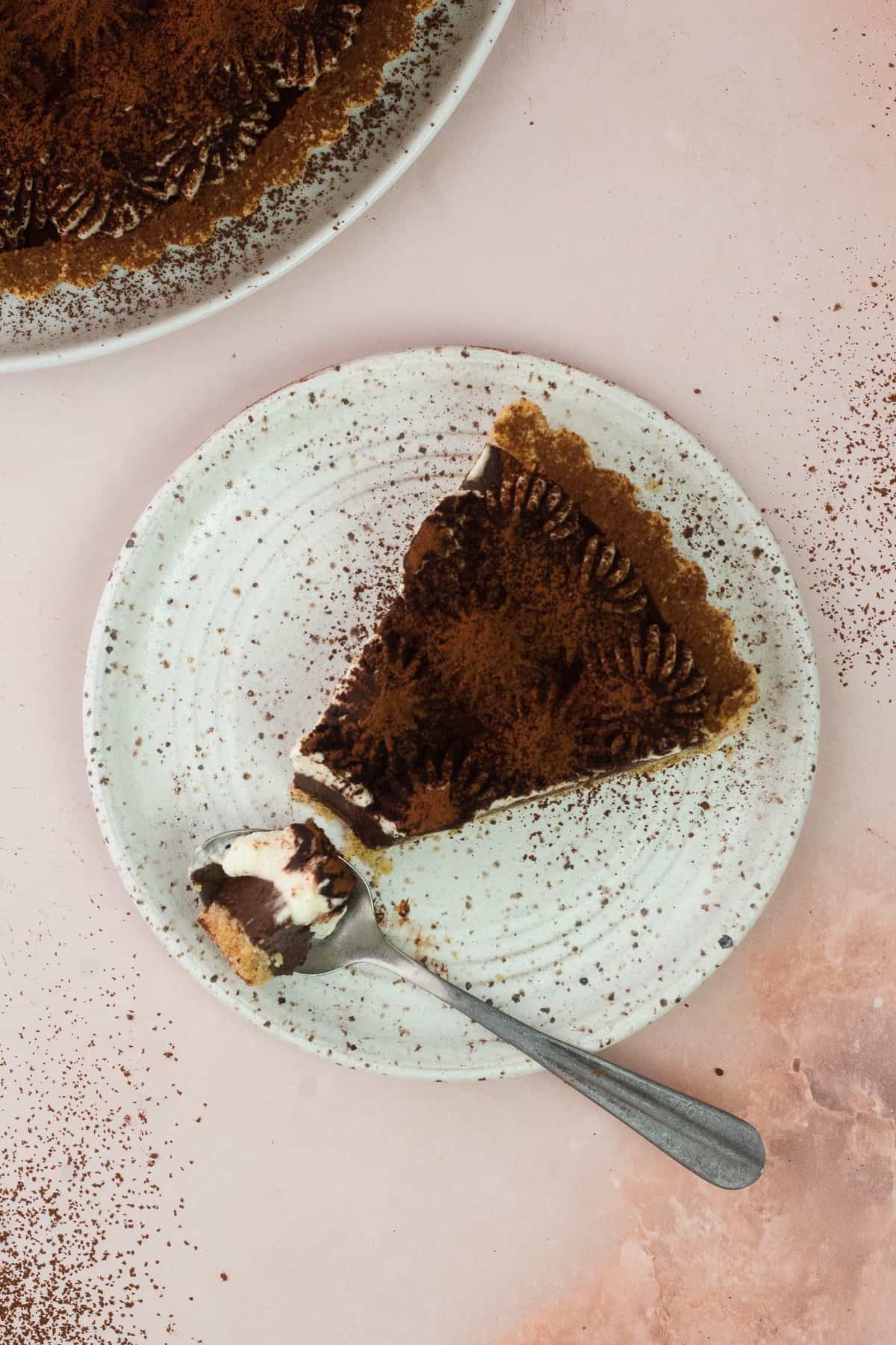 A slice of tiramisu tart on a plate with a spoon filled with a bit of tart