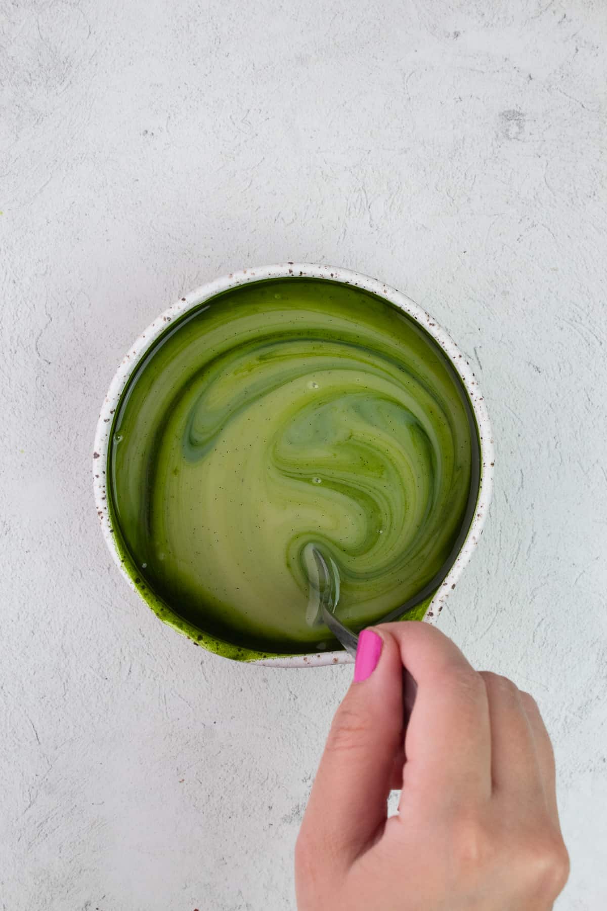 Bowl of condensed milk, vanilla, peppermint extract and matcha powder being mixed with spoon