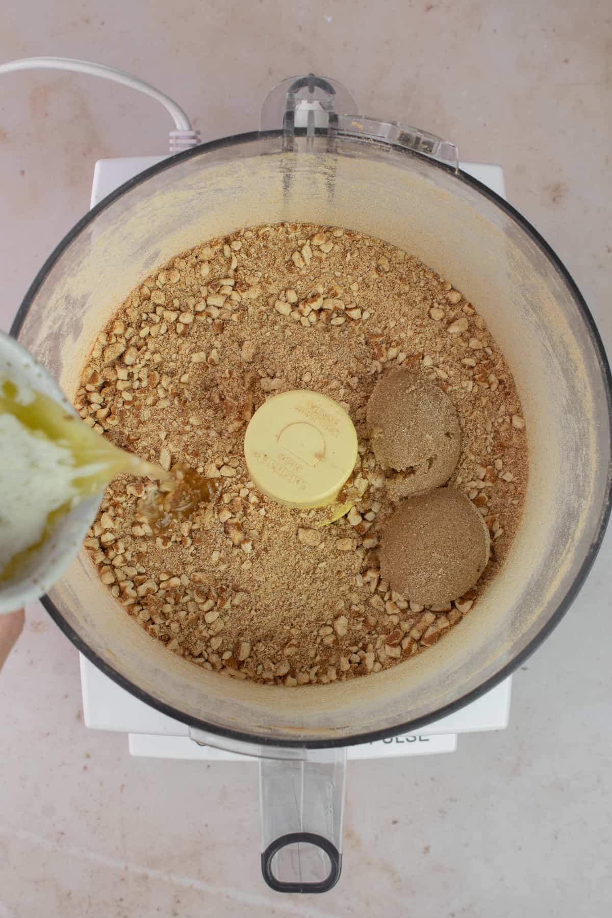 Food processor with crust pretzel crumbs, brown sugar and melted butter is being drizzled in