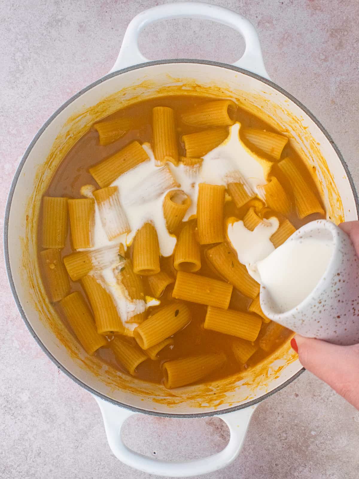 Pouring cream in cheesy pumpkin rigatoni pot