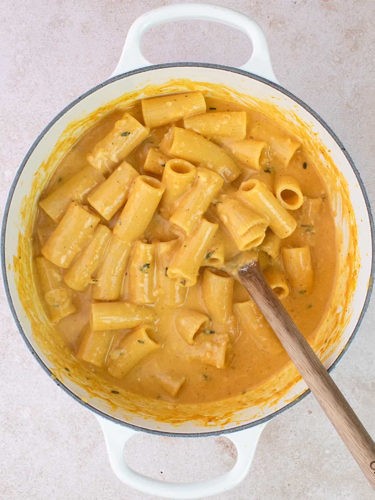 Cheesy pumpkin rigatoni in white pot with wooden spoon