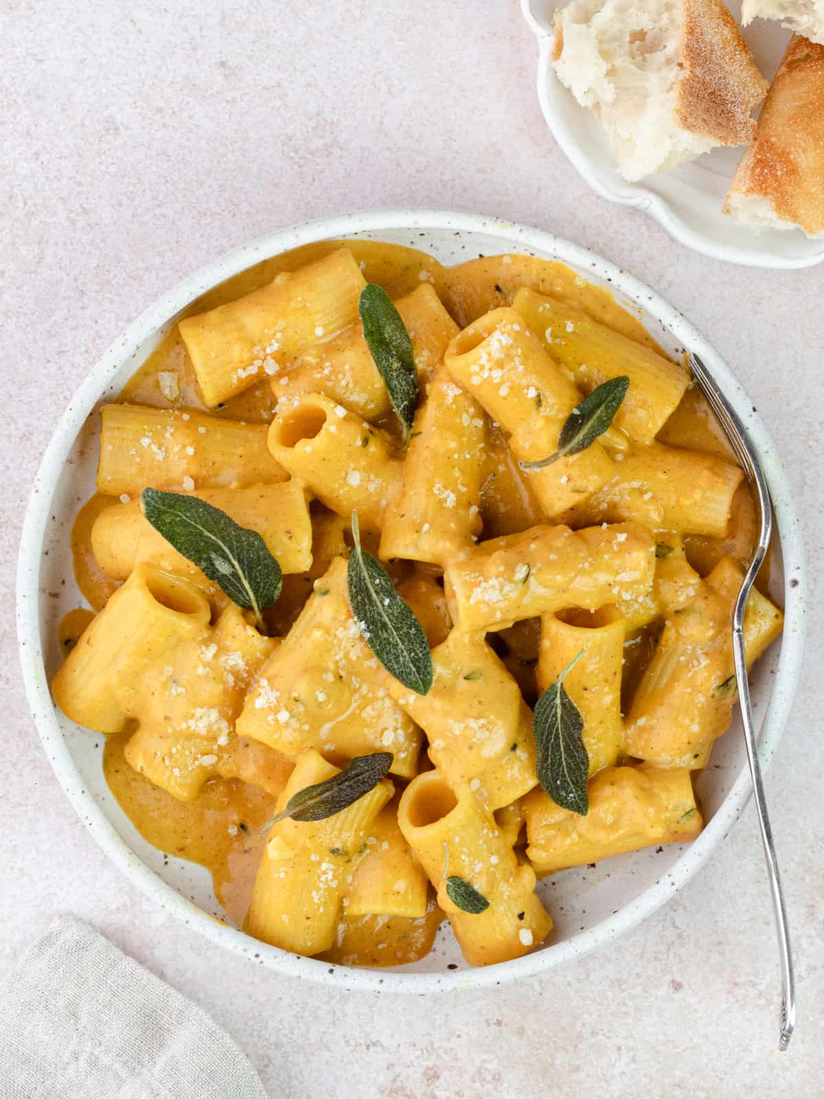 Cheesy pumpkin rigatoni with crisp sage leaves in a bowl with fork