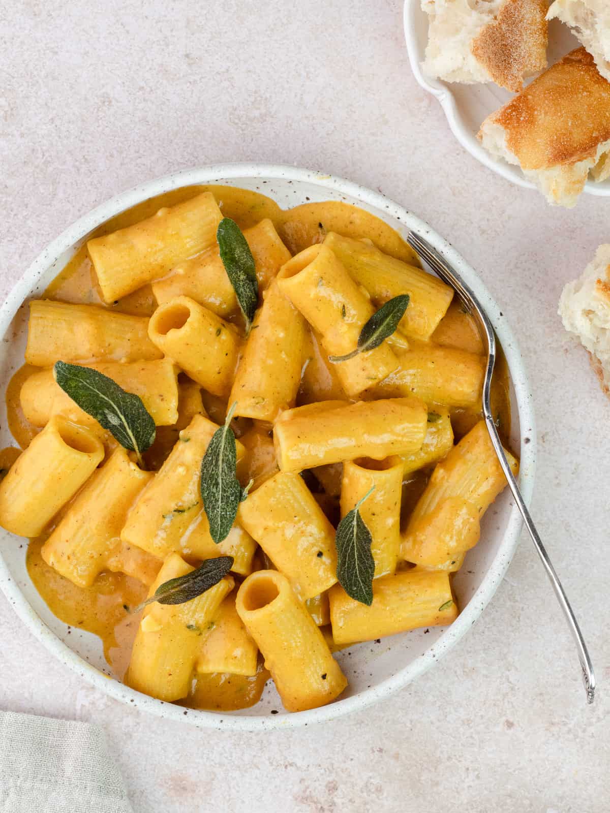 Cheesy pumpkin rigatoni with crisp sage leaves in a bowl with fork