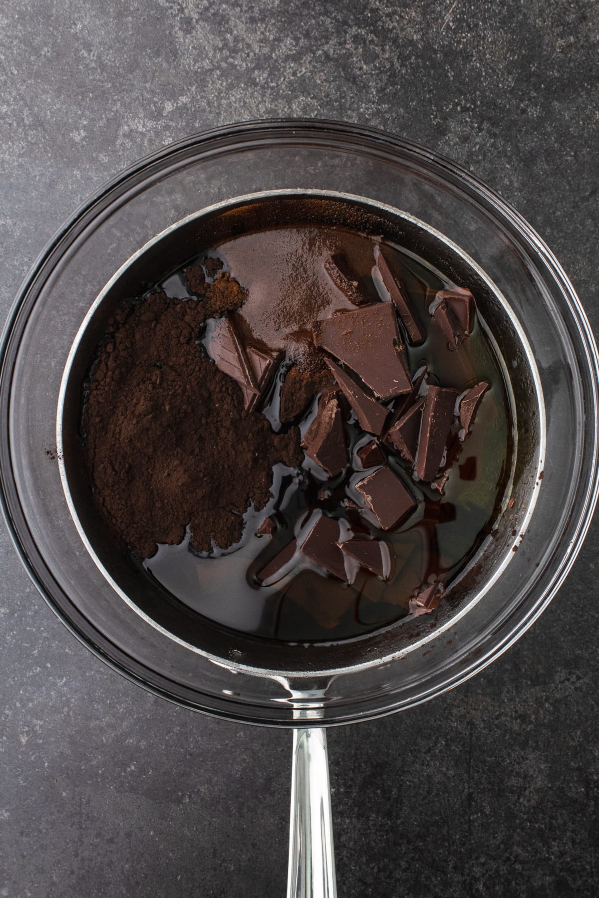 Chocolate, cocoa powder, espresso powder and olive oil in a glass bowl over a saucepan of simmering water