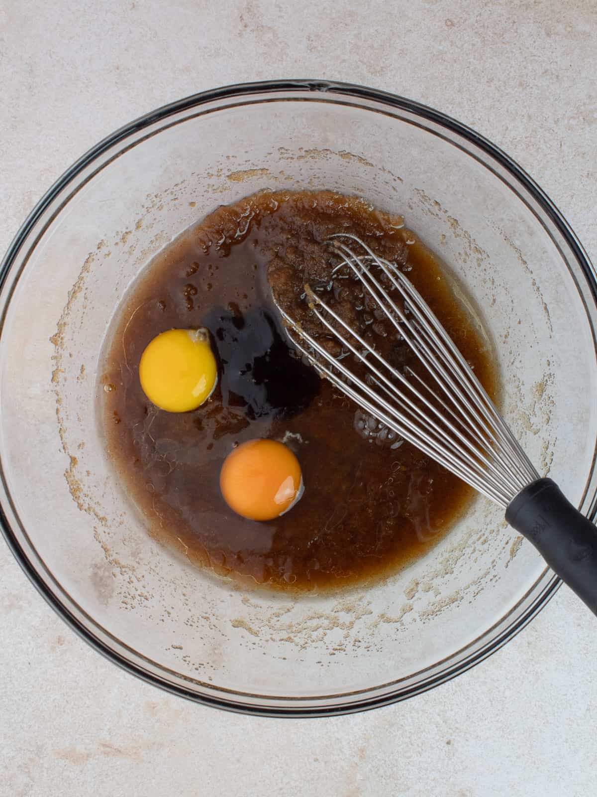 Brown butter, brown sugar, egg, yolk and vanilla are in a large glass mixing bowl with a whisk