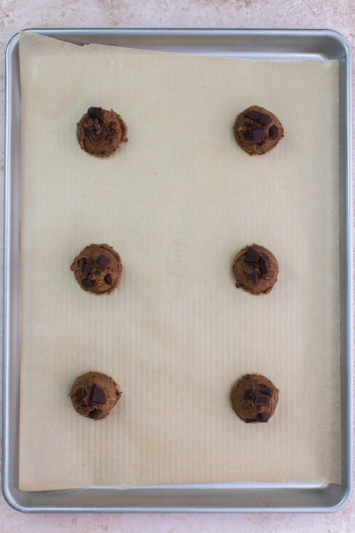 Six raw cookie dough balls on baking sheet