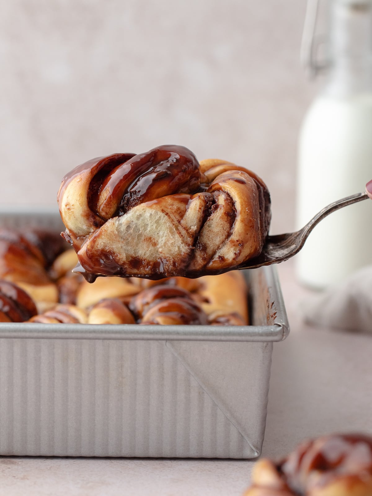 Cake server holding a piece of Nutella knot bun over a tray of buns