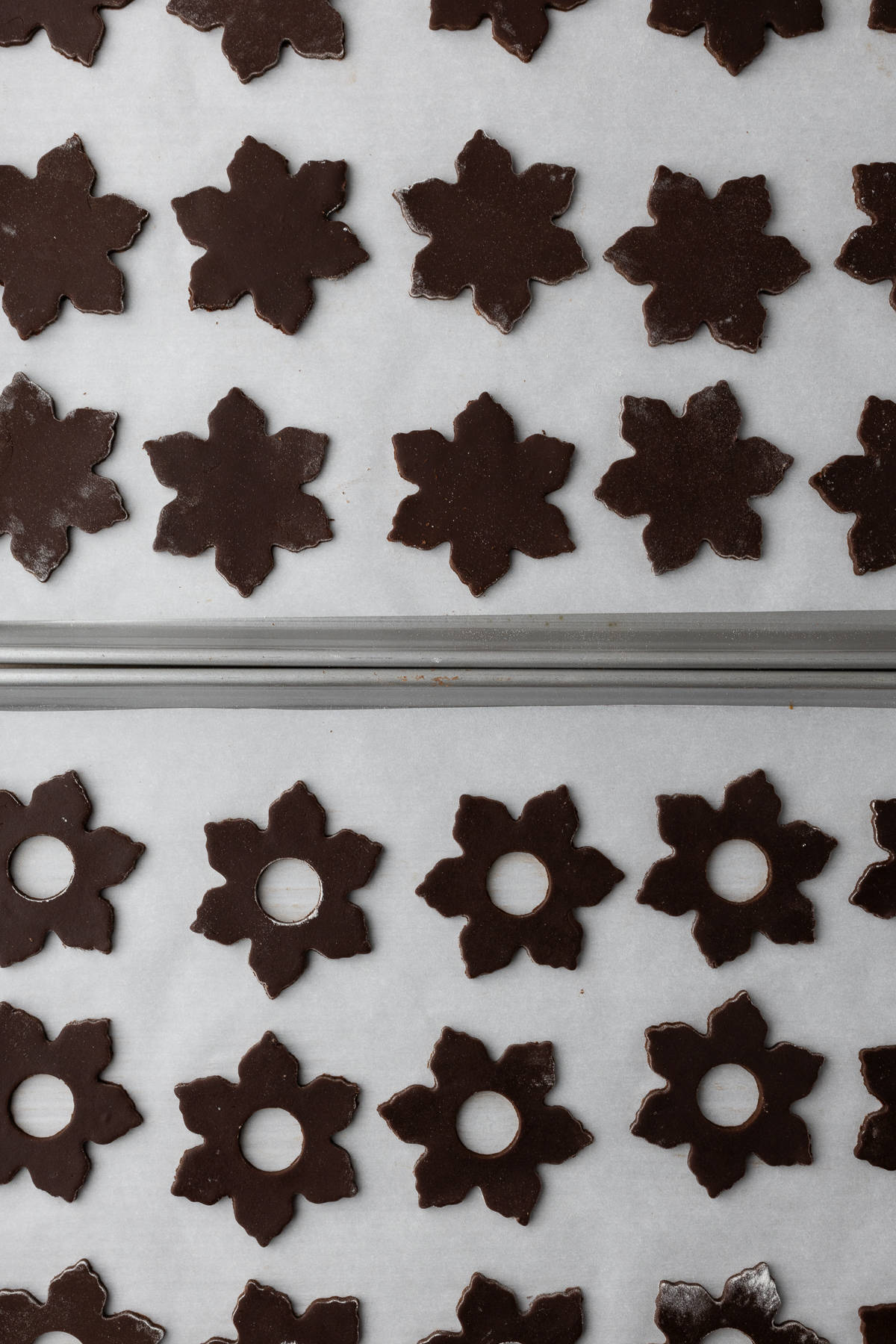 Chocolate linzer cookies cut out into snowflake shape and placed on baking trays