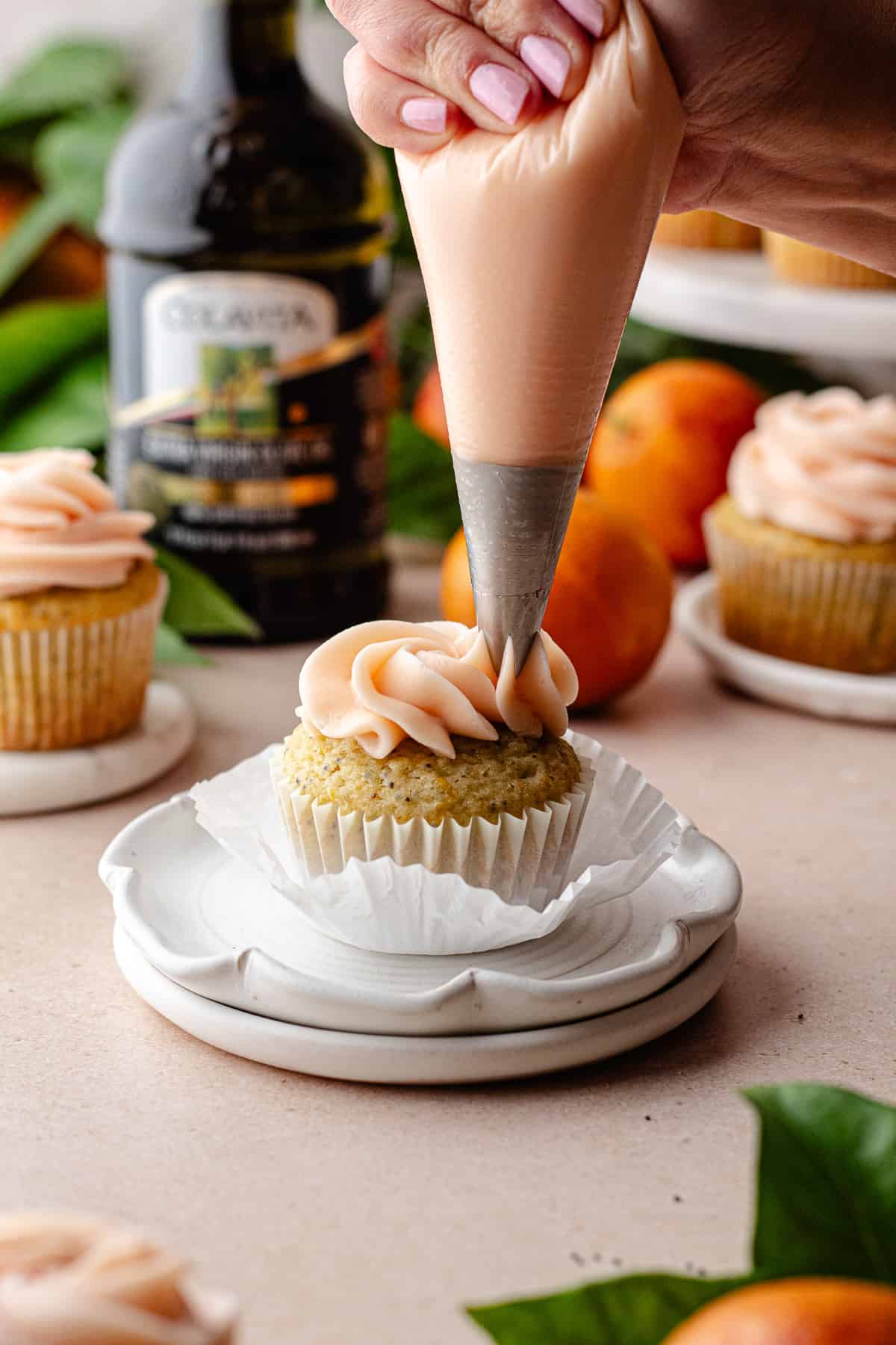 Piping cream cheese frosting onto a cupcake.