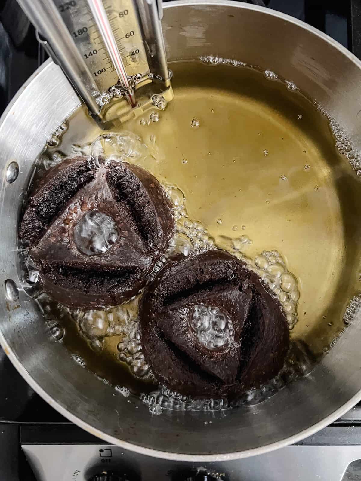Two chocolate donuts are frying in a pot of oil.