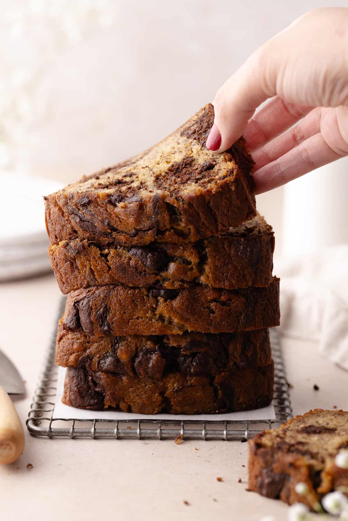 Hand grabs a slice of chocolate marbled banana bread sliced on wire rack.