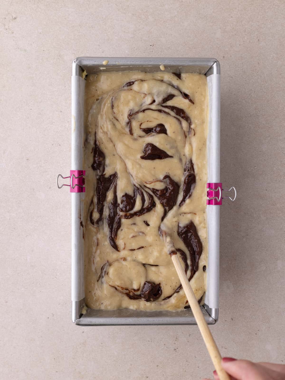 Chopstick swirling banana batter and chocolate batter together in loaf pan.