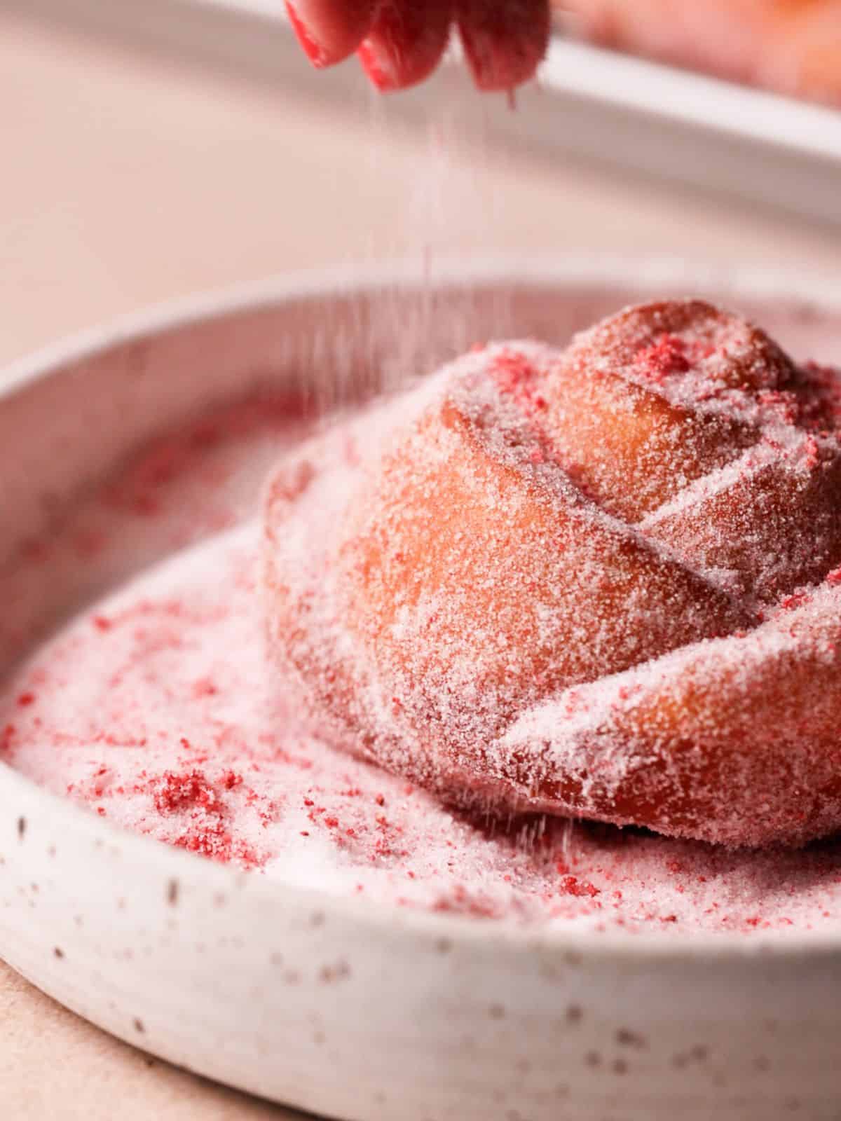 Coating rose donuts in strawberry sugar.