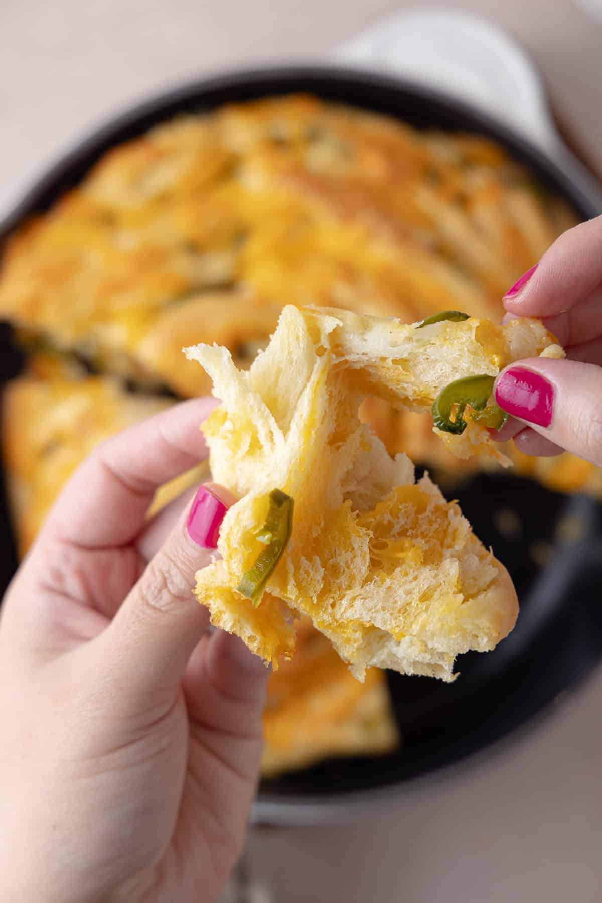 Hands holding a piece jalapeno cheddar twist bread, showing light fluffy texture.