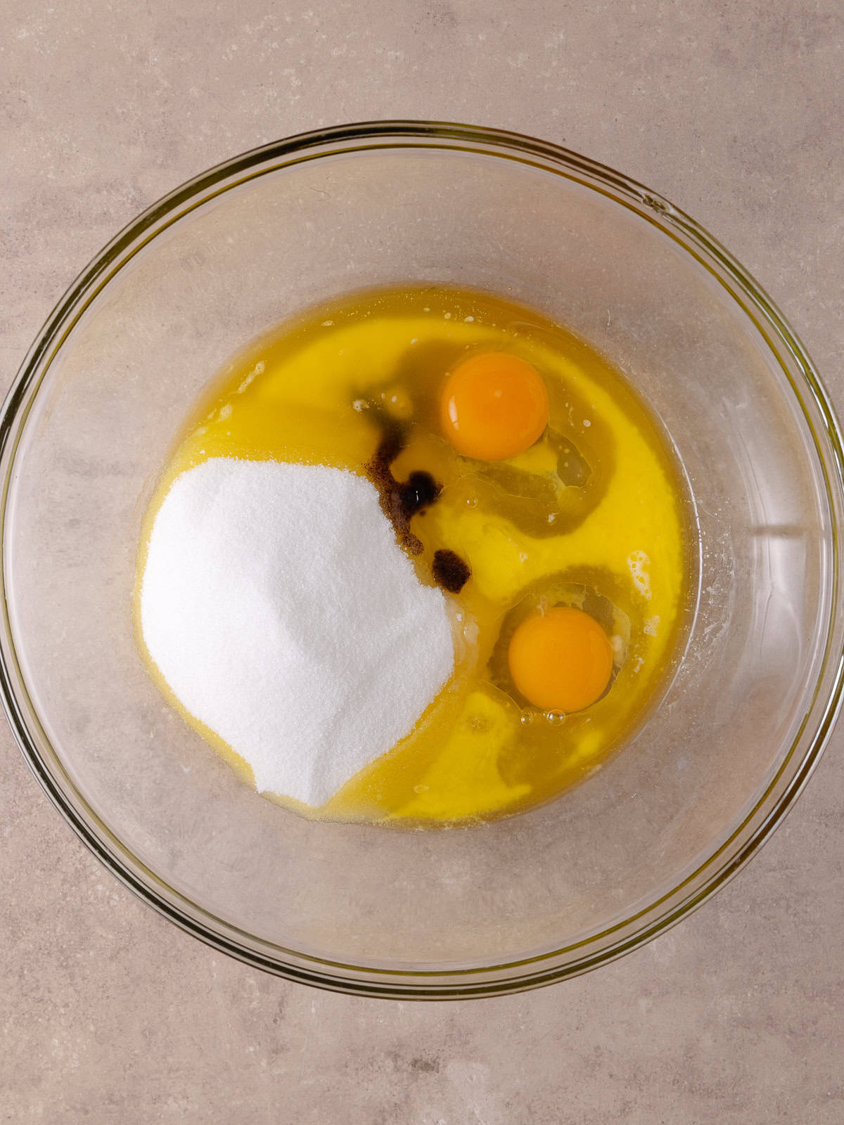 Melted butter, whole eggs, white sugar and vanilla are added to a large glass mixing bowl.