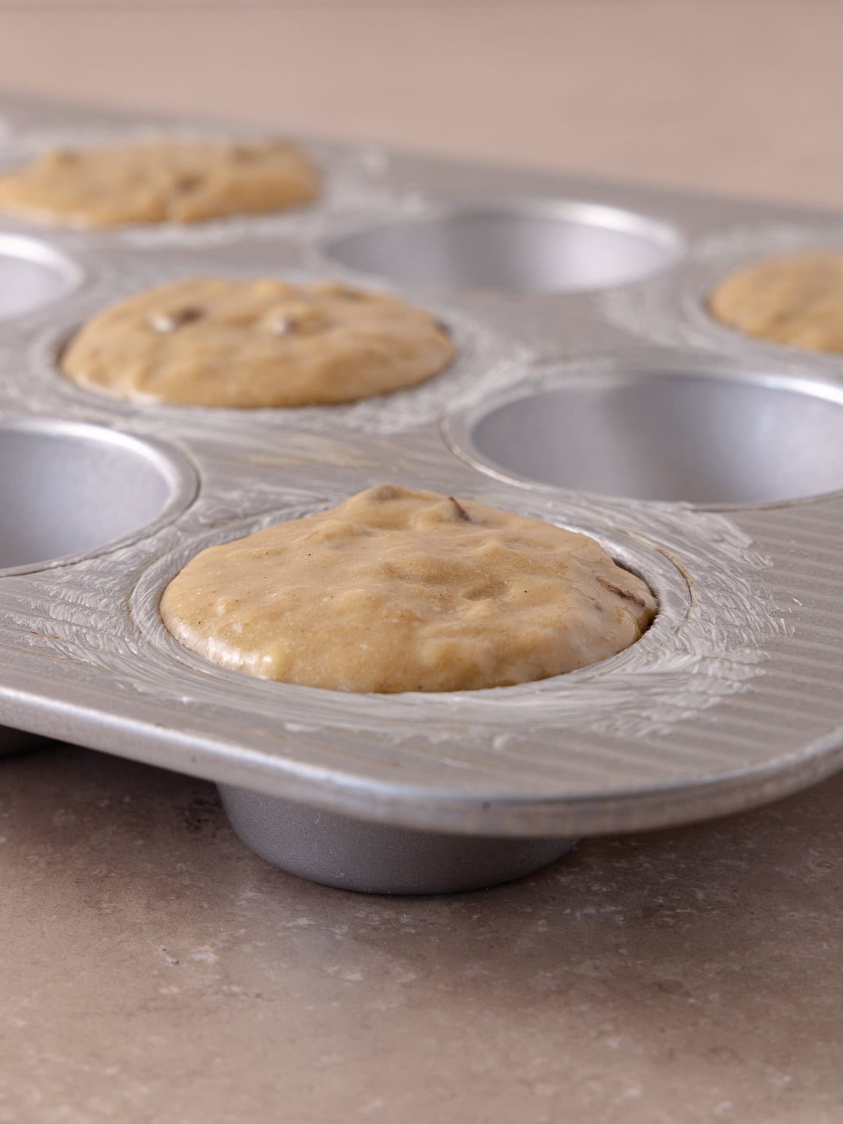 Muffin batter is poured in every other cavity of a muffin pan.
