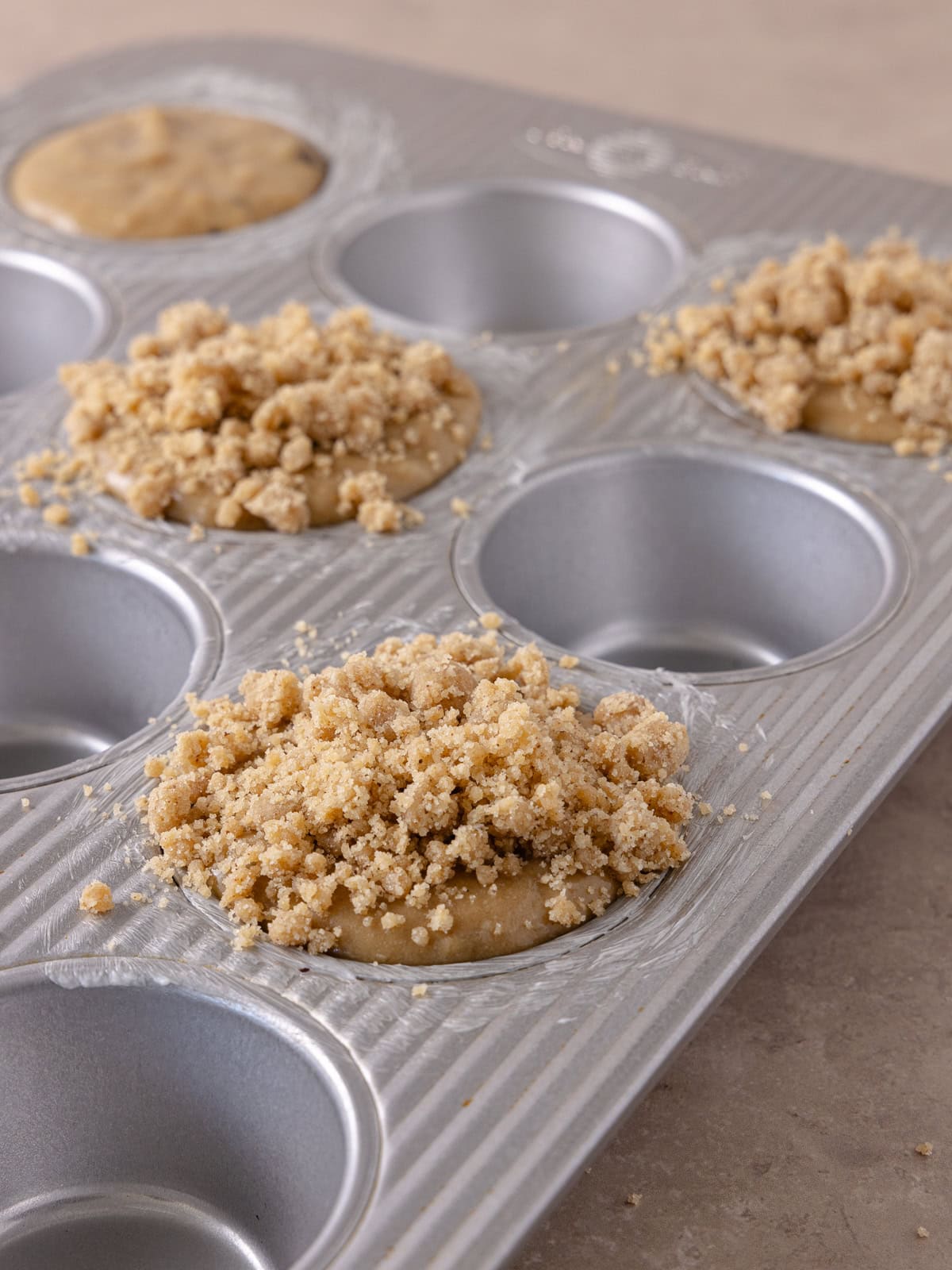 Muffin batter and streusel topping poured in every other cavity of a muffin pan and is now ready to bake.
