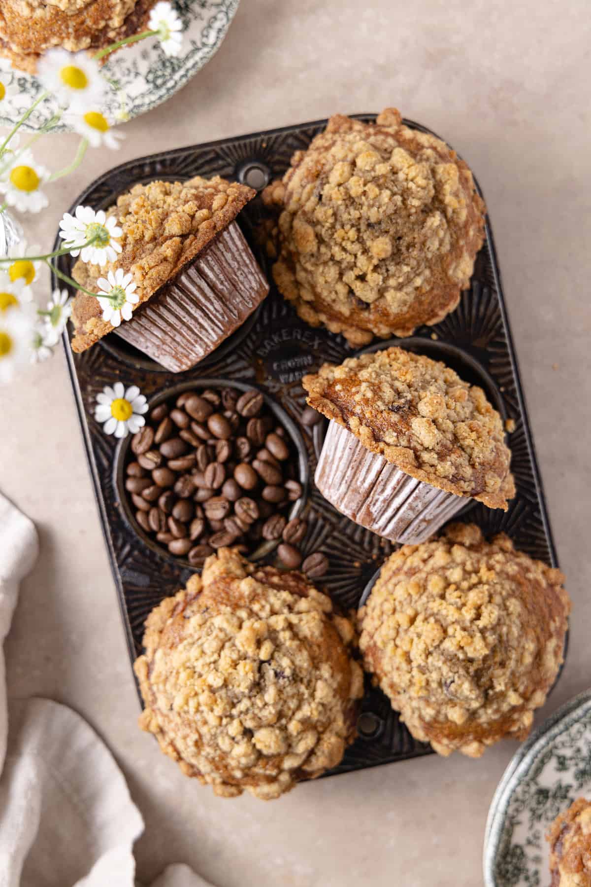 Banana Espresso Muffins in a 6-cup muffin pan, with plates all around and a beige napkin in the bottom left corner.