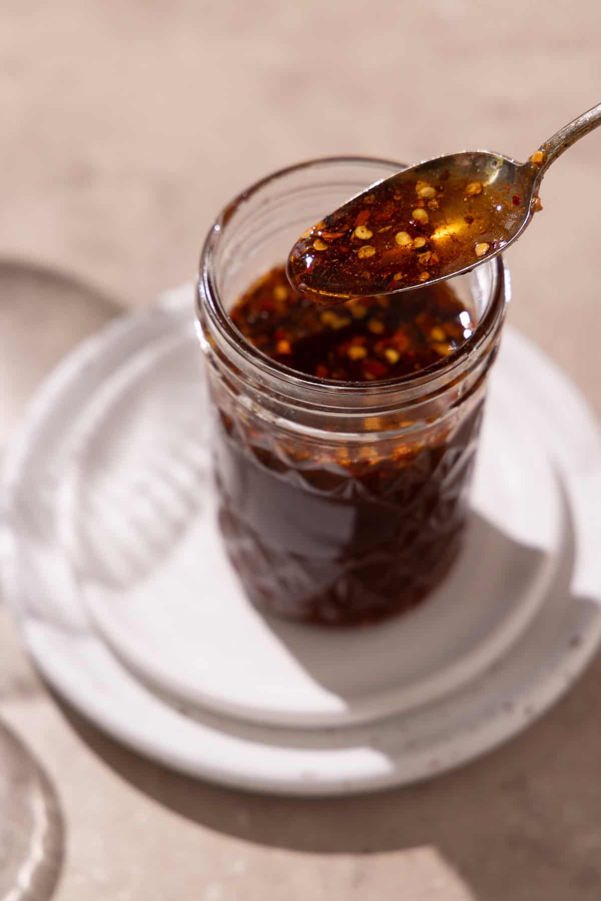 Hot honey is in a mason jar on top of 2 plates. A hand holds a spoon with hot honey.