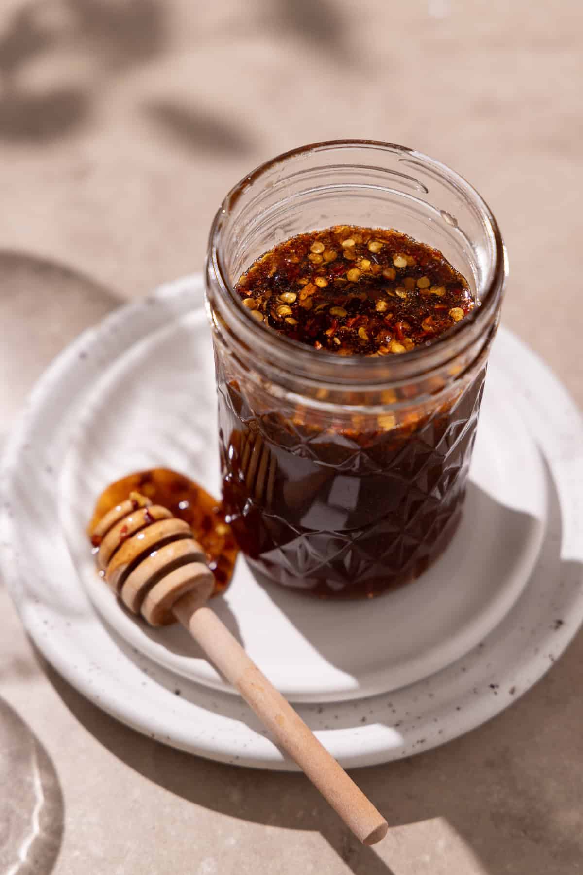 Hot honey is in a mason jar on top of 2 plates. A honey dipped sits next to the jar.
