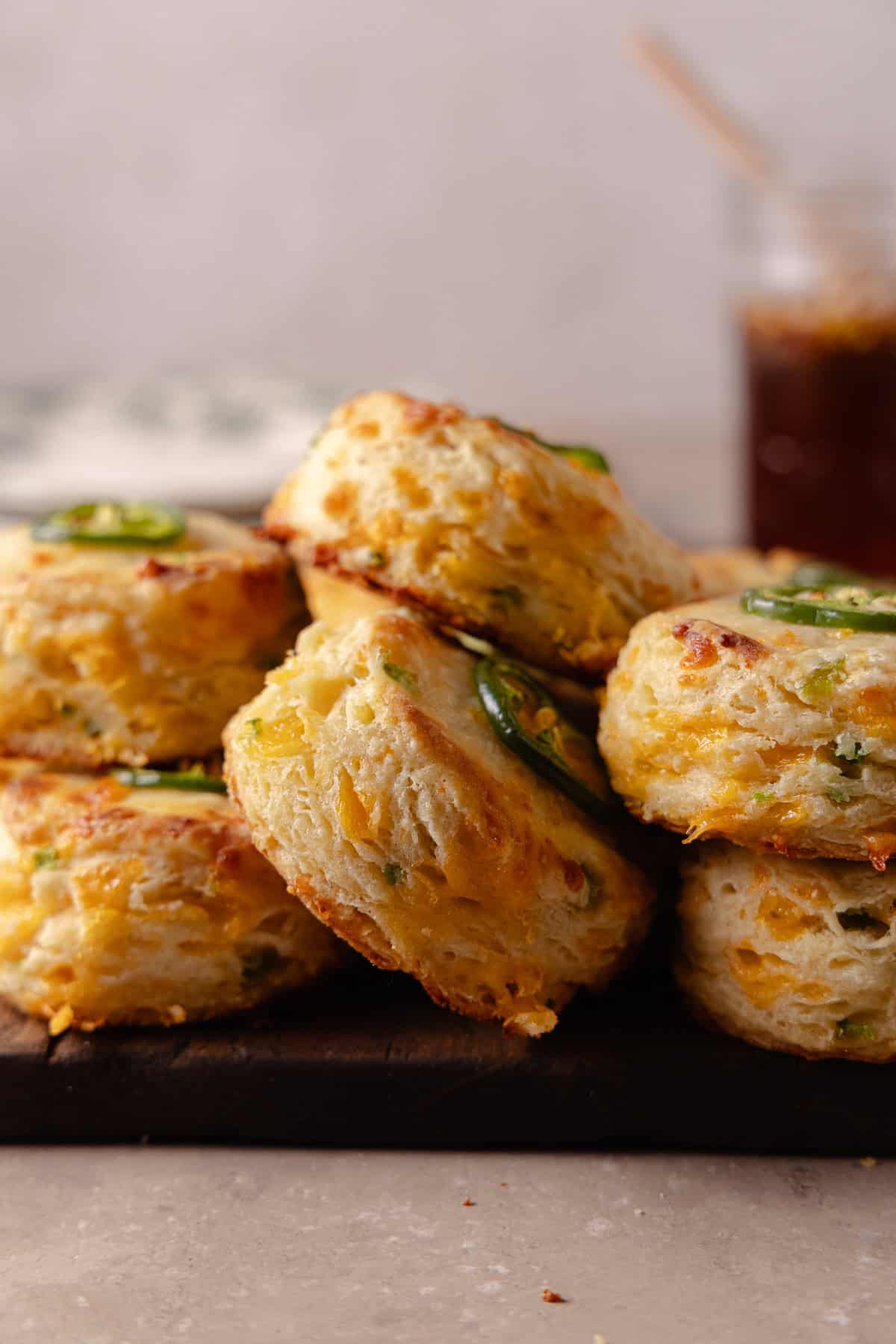 A pile of Jalapeno Cheddar Biscuits on a cutting board with a glass jar of hot honey in the corner.