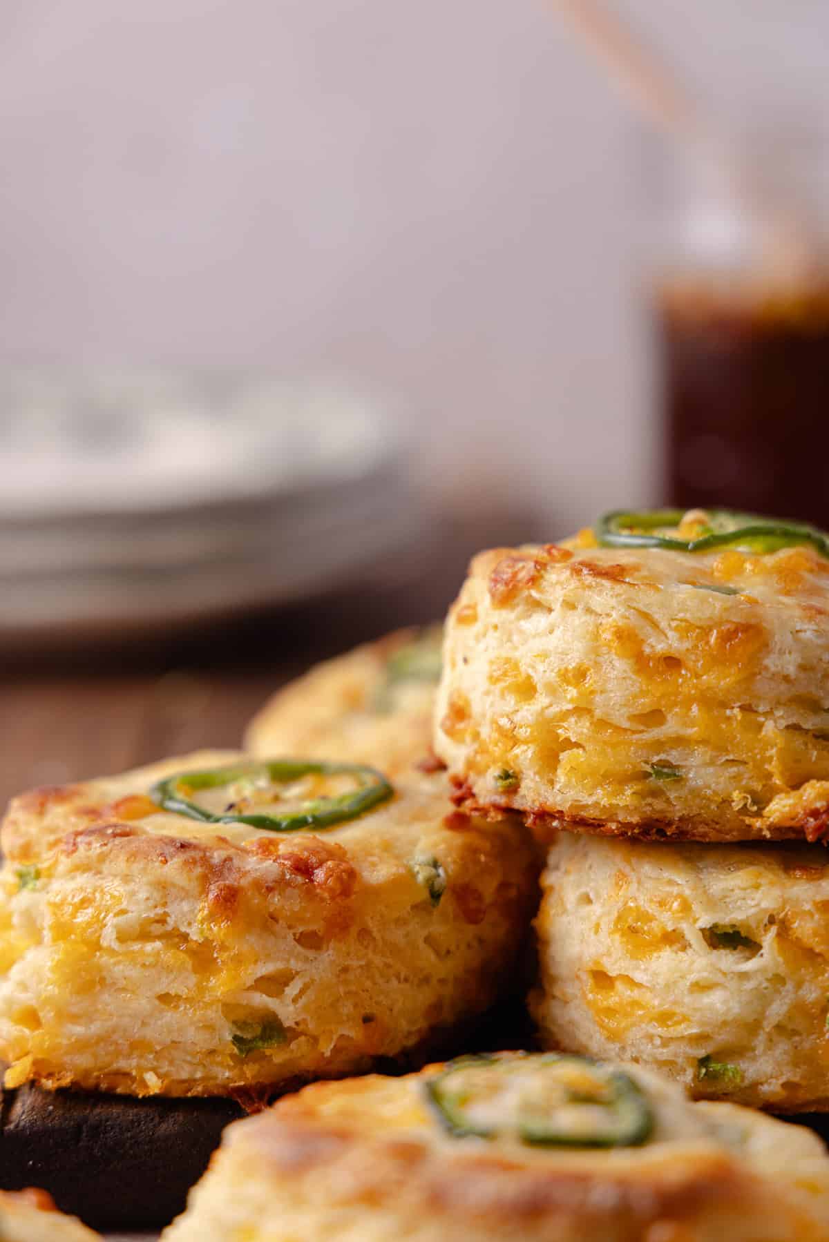 A close up of a pile of Jalapeno Cheddar Biscuits on a cutting board with a glass jar of hot honey in the corner.