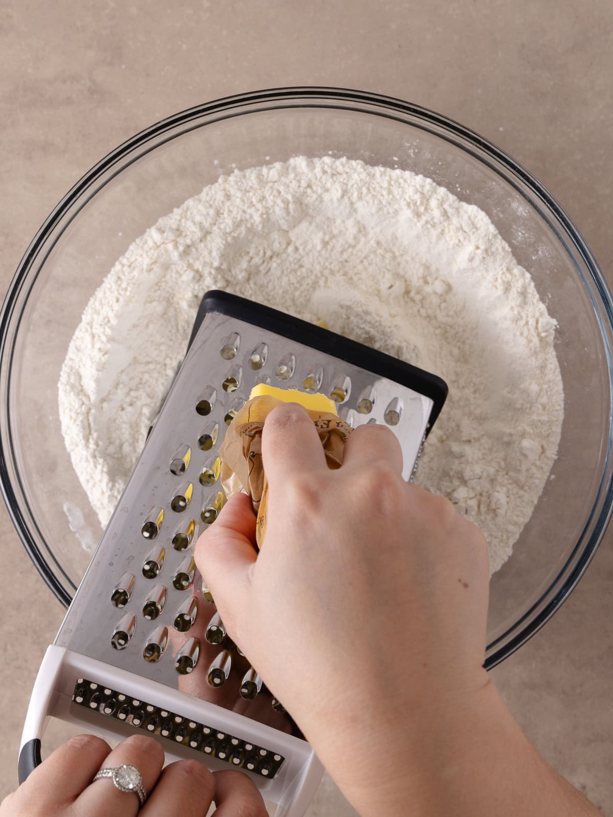 A hand grates frozen butter with a box grater into the bowl with the flour mixture.