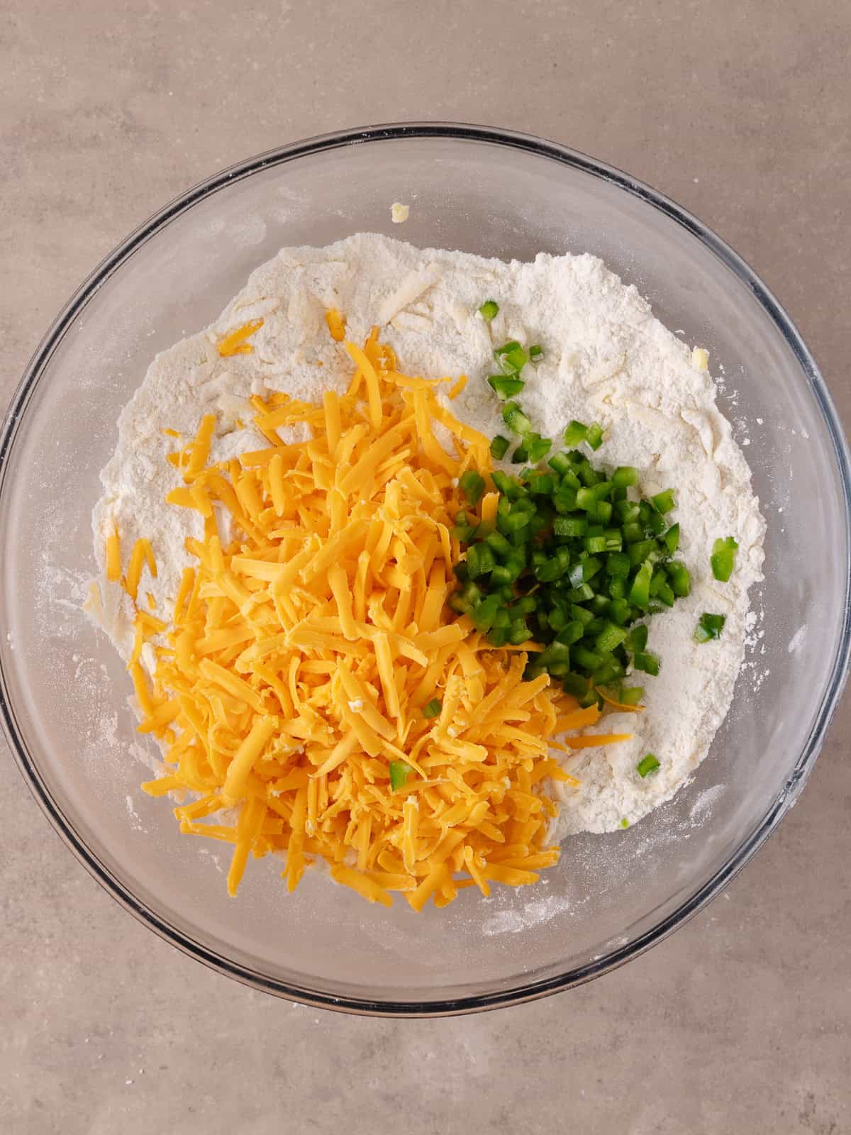 Shredded cheddar cheese and finely chopped fresh jalapenos are added to the bowl with the flour mixture.