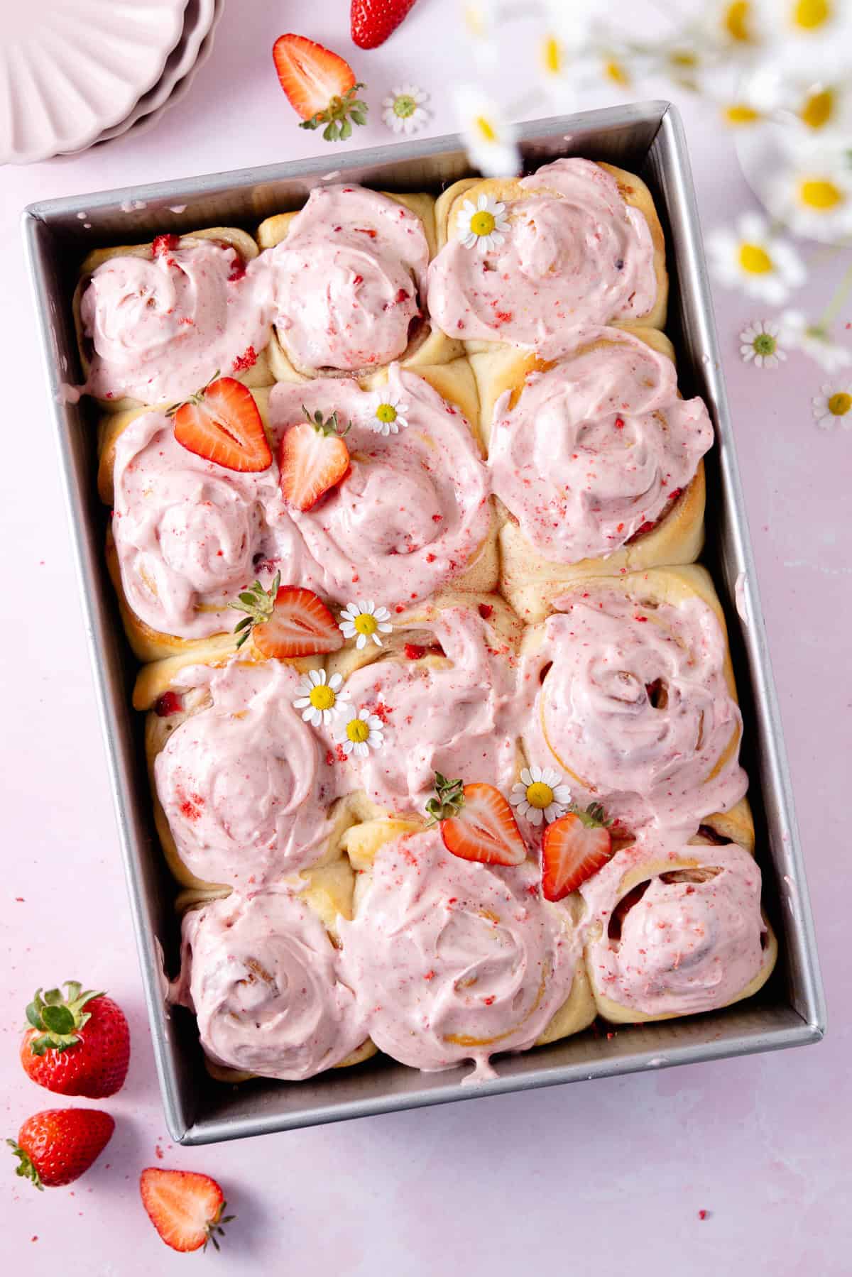 A large baking dish with frosted Strawberry Cinnamon Rolls and fresh strawberries.