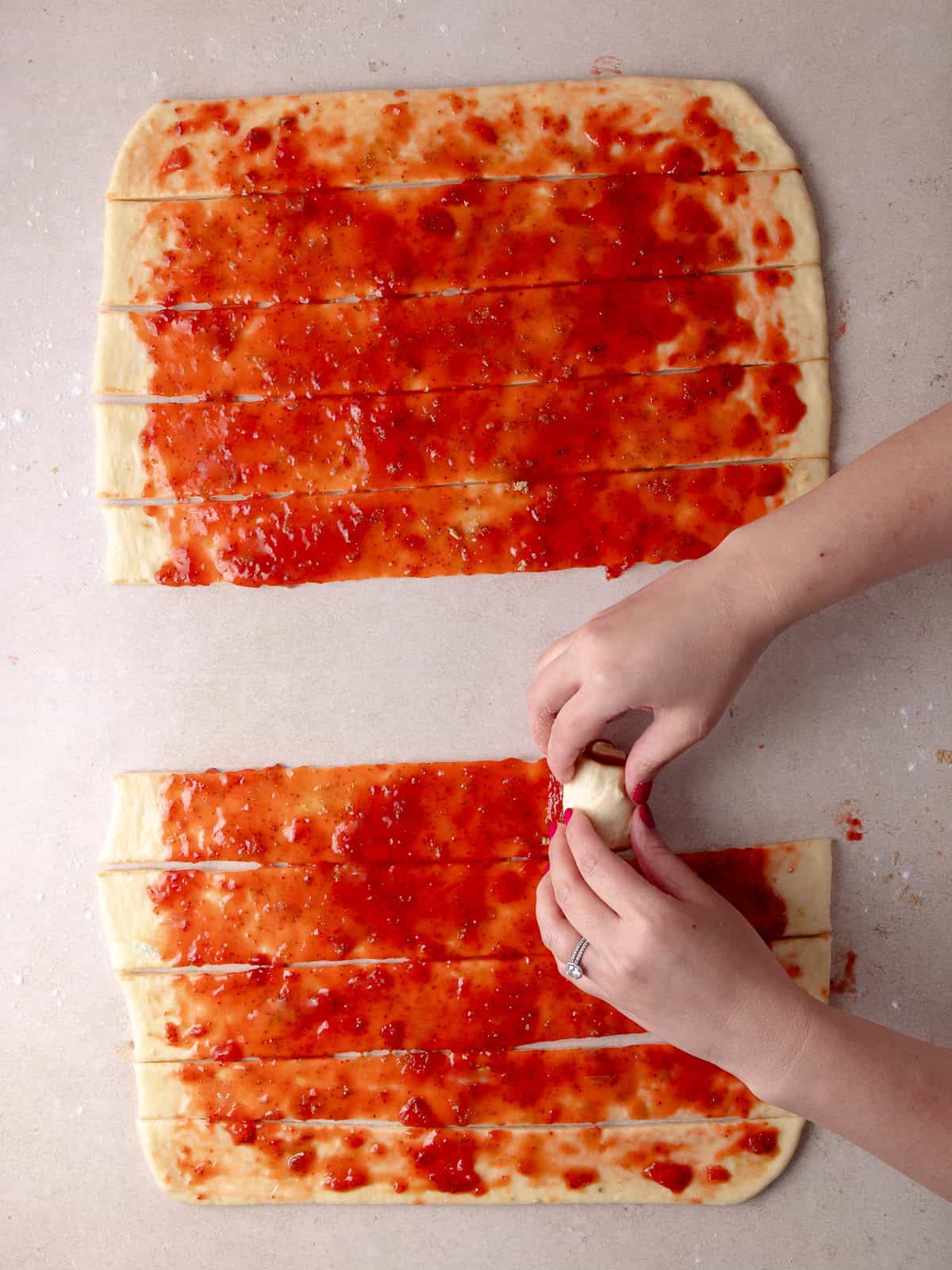 Hands are rolling the strips of dough into buns.