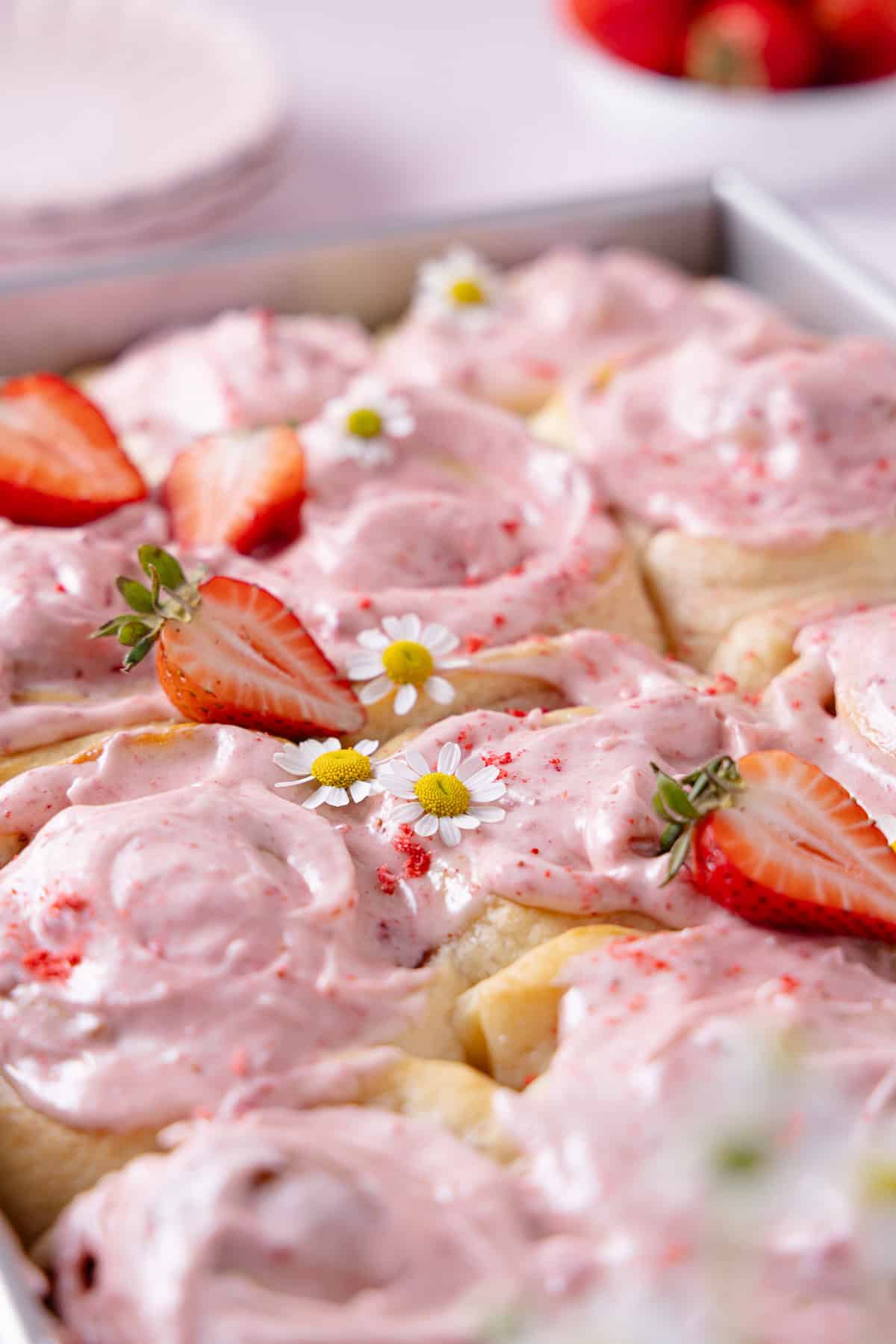 Frosted Strawberry Cinnamon Rolls in a baking tray garnished with fresh strawberries and flowers.