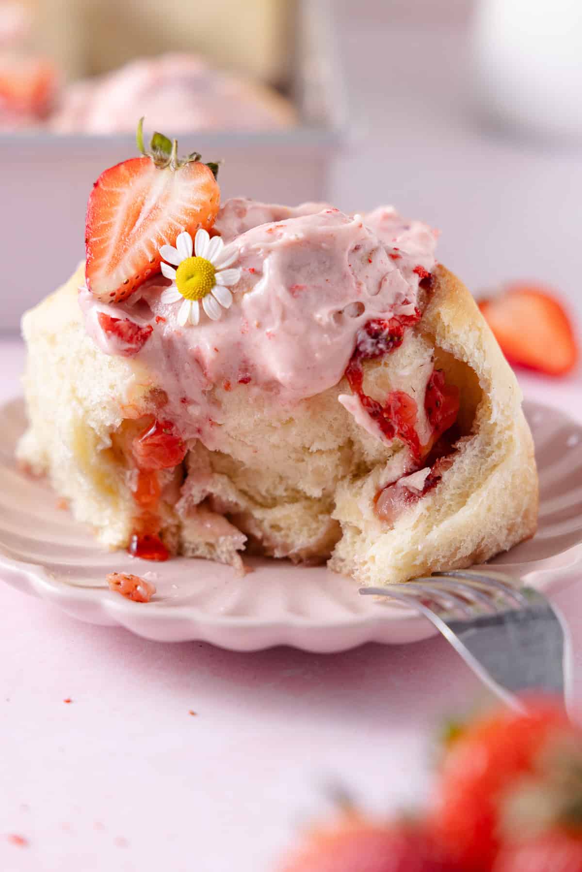 Frosted Strawberry Cinnamon Roll on a small pink fluted dish with a fork.