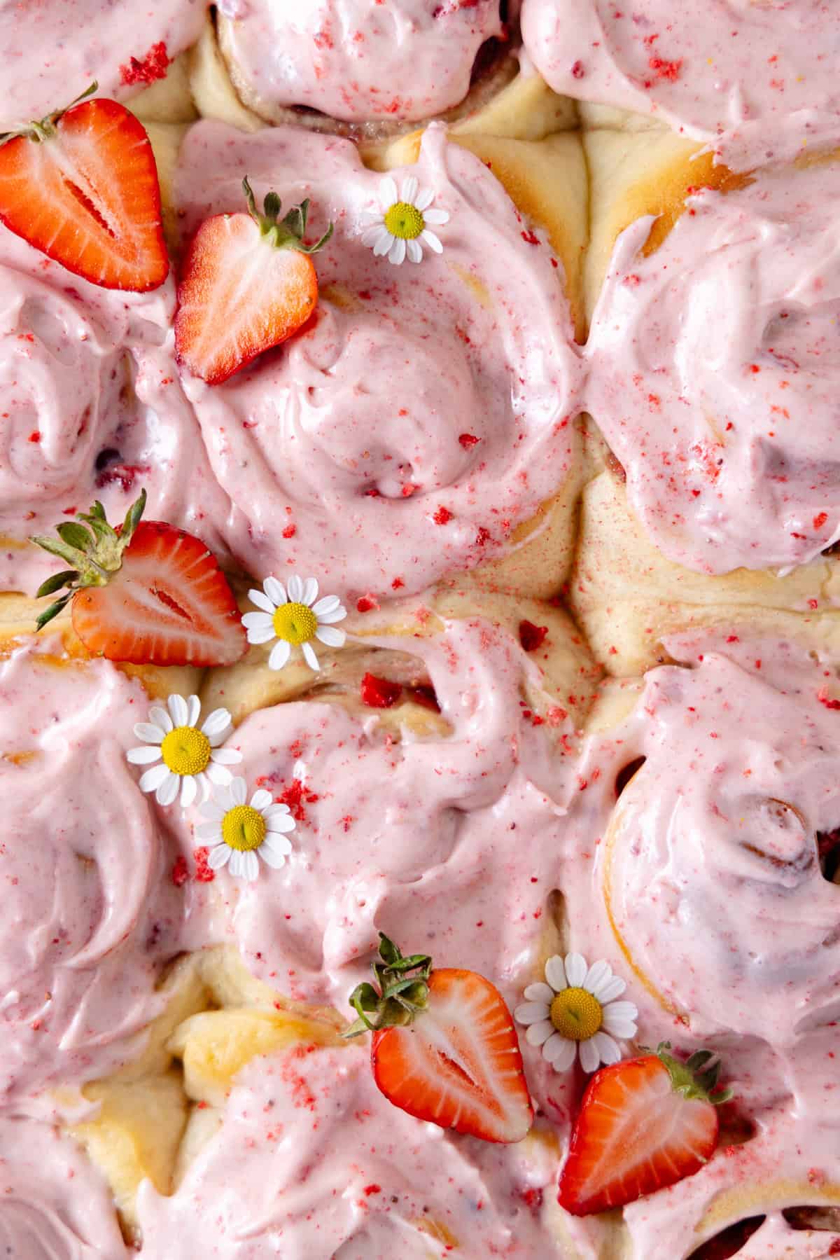 Close up of a large baking dish with frosted Strawberry Cinnamon Rolls and fresh strawberries.