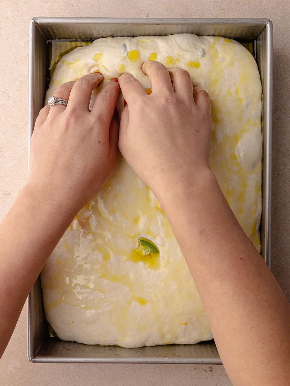 Hands and dimpling the focaccia dough in the baking pan.