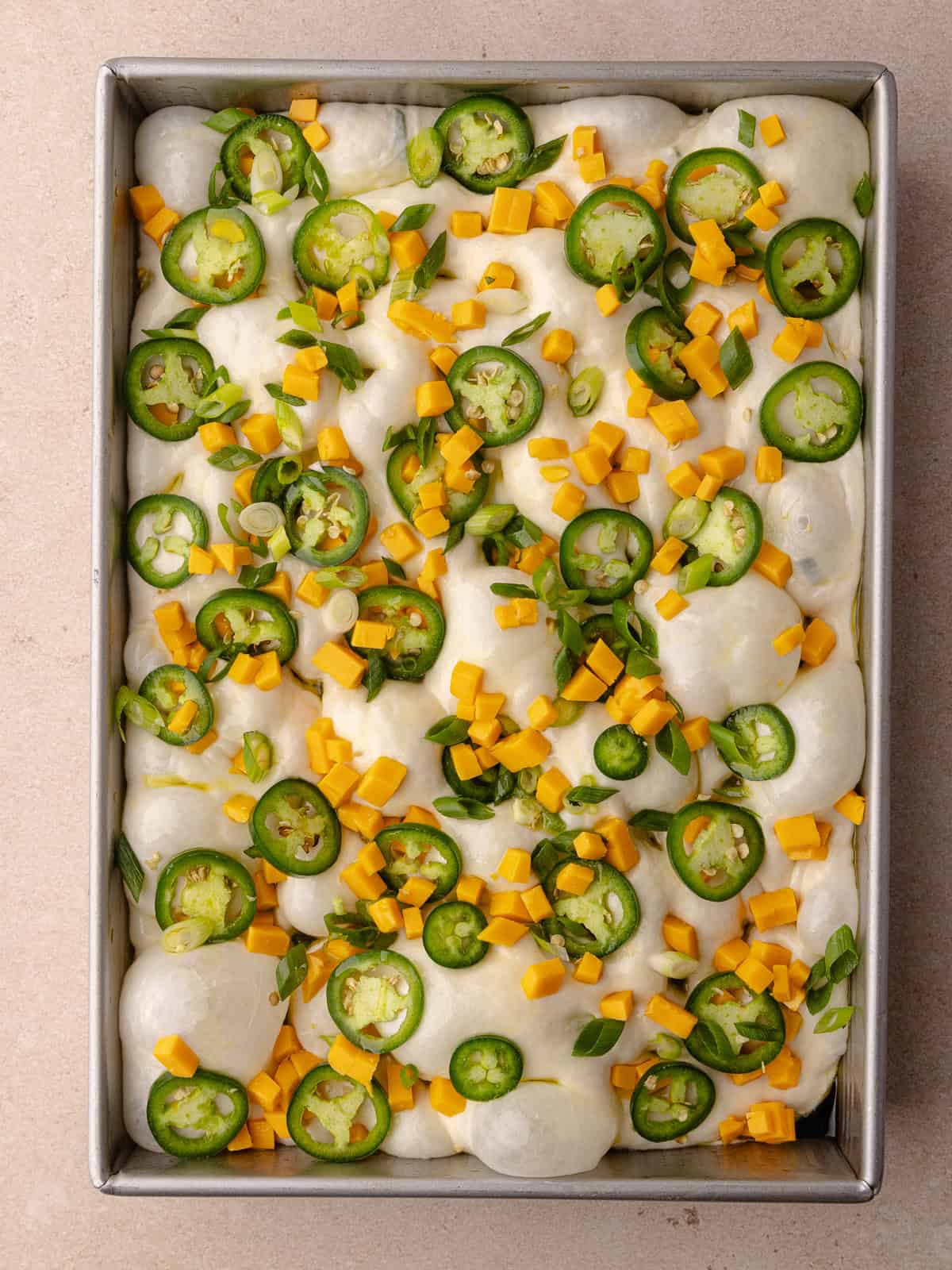 Chunks of cheddar cheese, sliced jalapenos and green scallions are added on top of the dough.
