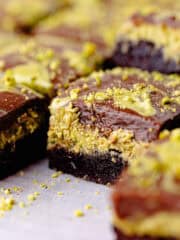 Pistachio brownies filled with kataifi pistachio cream filling are cut into squares and are sitting on a wire rack feature photo.