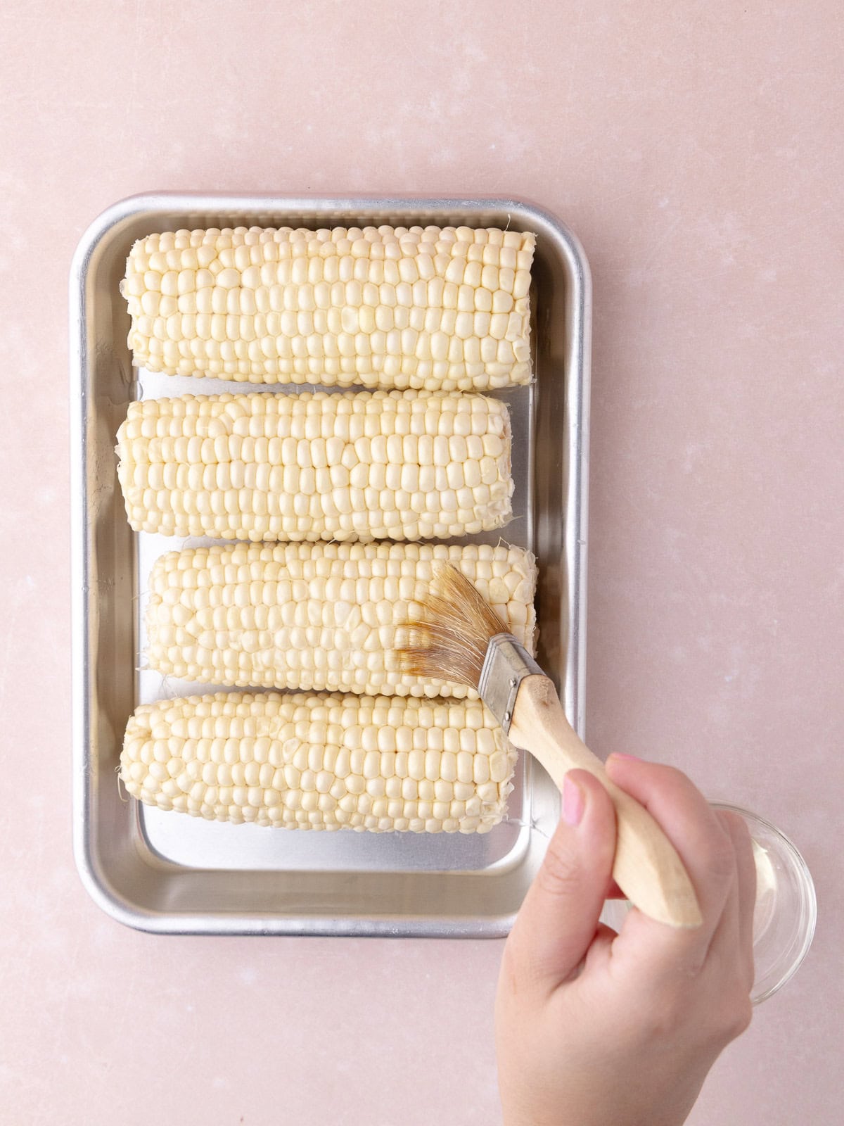 Cooking oil is brushed on the corn on the cob.