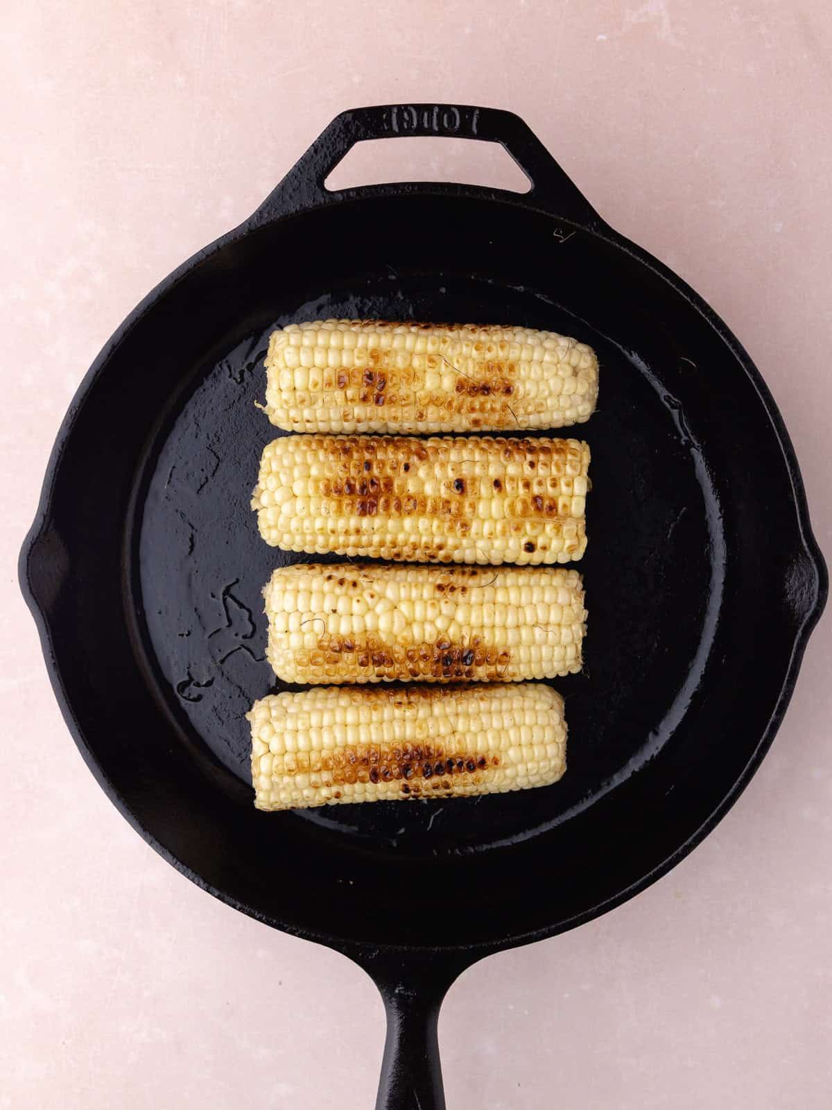 Four fresh corn on the cob is charred in a large cast iron pan.