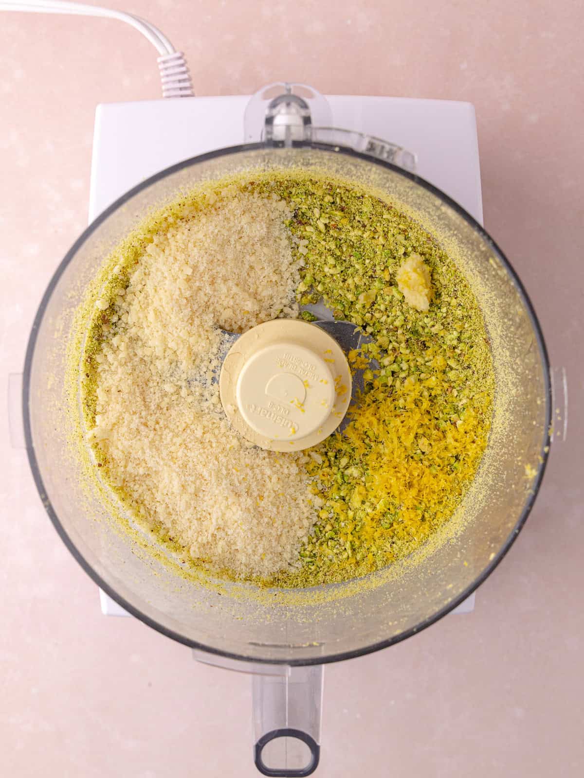 Parmesan cheese, grated lemon zest and grated garlic is added in food processor bowl with the ground pistachios.