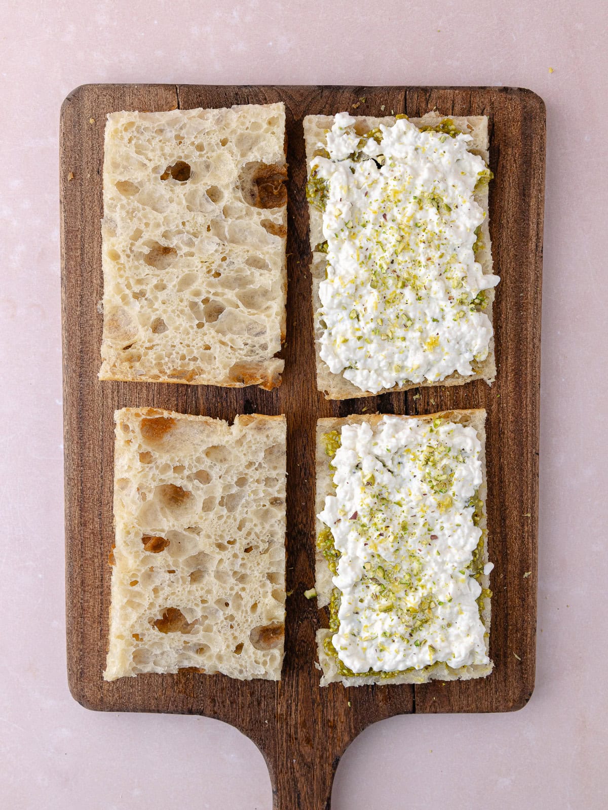 Pistachio cream and stracciatella cheese is spread on half of a schiacciata, then topped with lemon zest and crushed pistachios.
