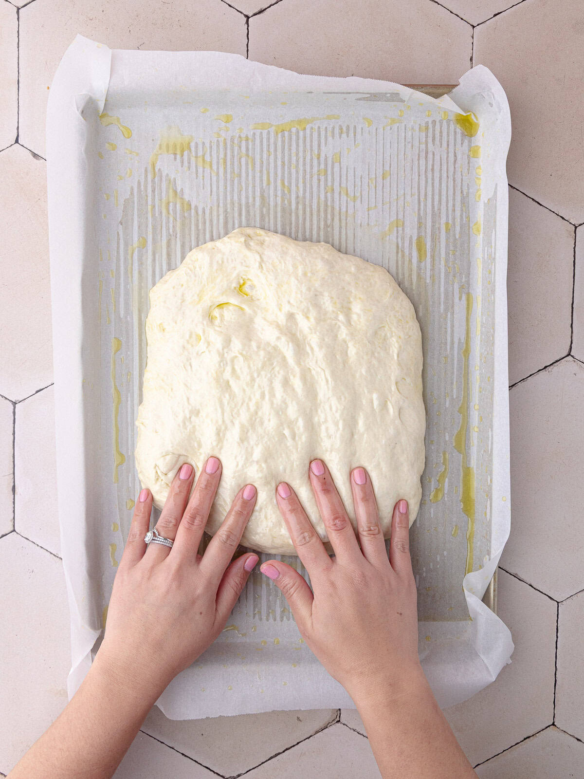 Schiacciata bread dough is stretched in a large baking sheet lined with parchment paper.