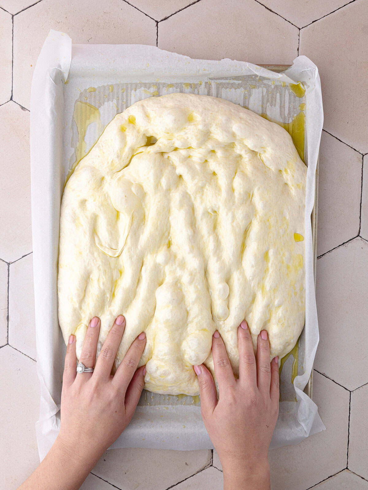 Schiacciata bread dough is stretched and dimpled in a large baking sheet lined with parchment paper.