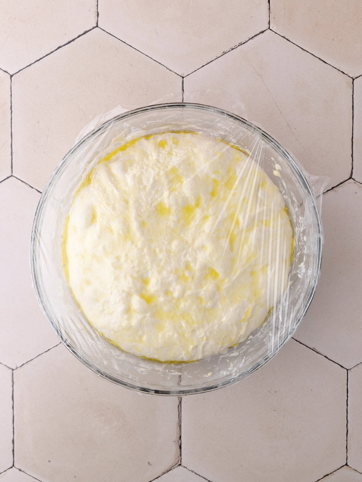 Schiacciata recipe dough is in a large glass mixing bowl and covered with plastic wrap.
