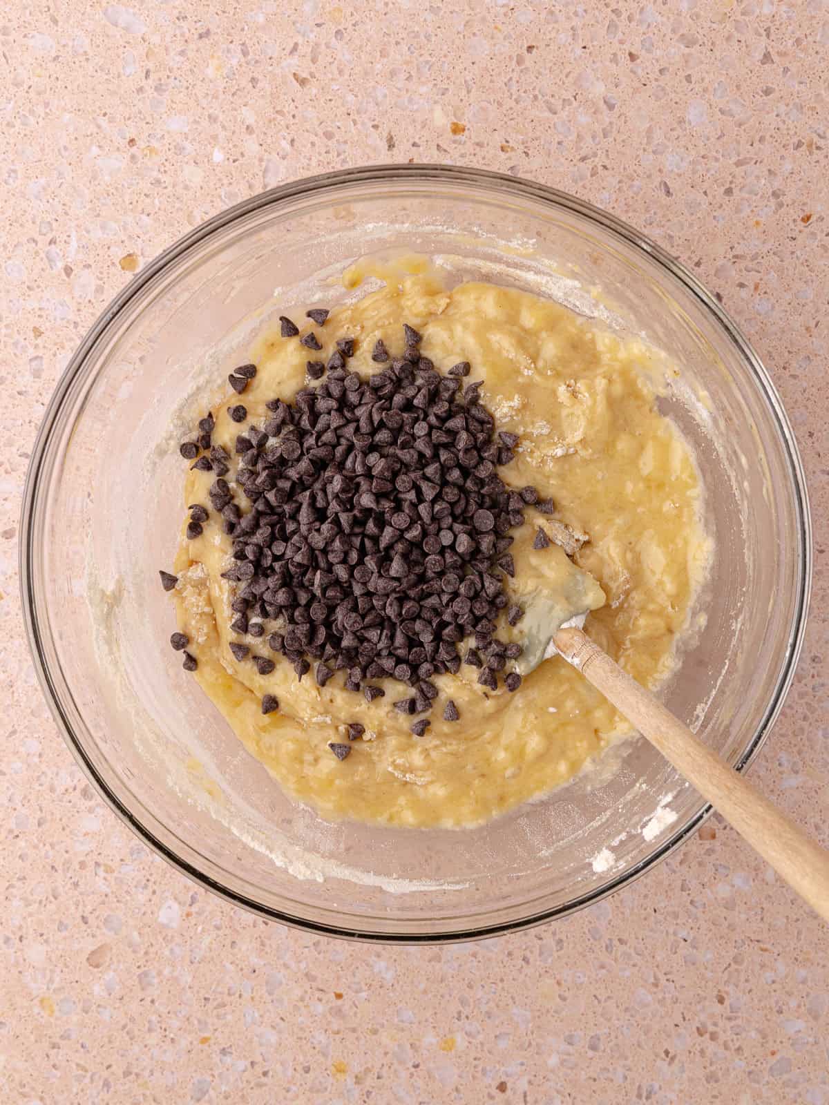 Mini chocolate chips are added to the banana batter sitting in a mixing bowl.